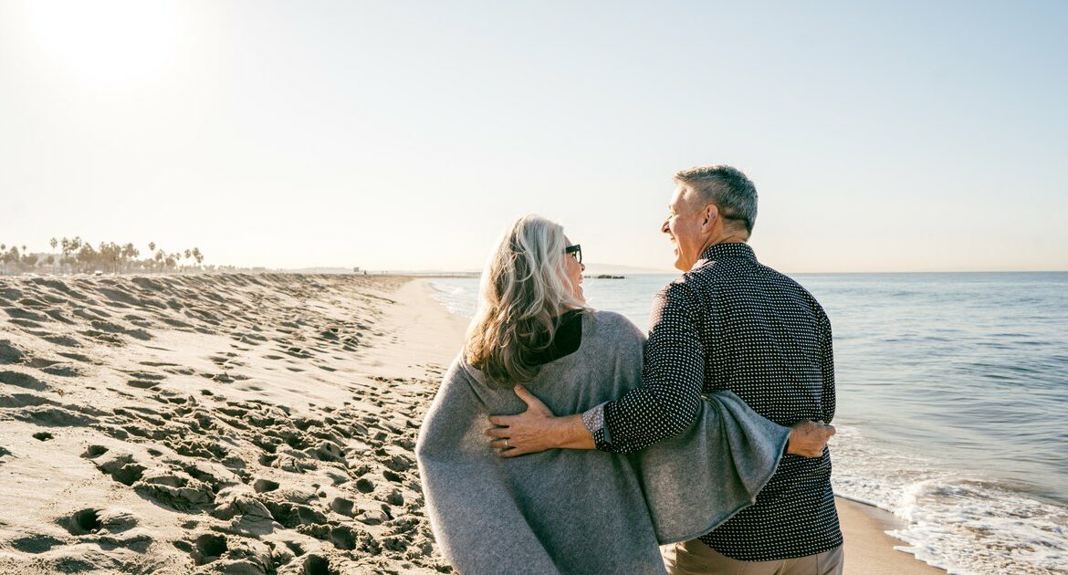 Un couple de seniors regarde la mer depuis une plage.