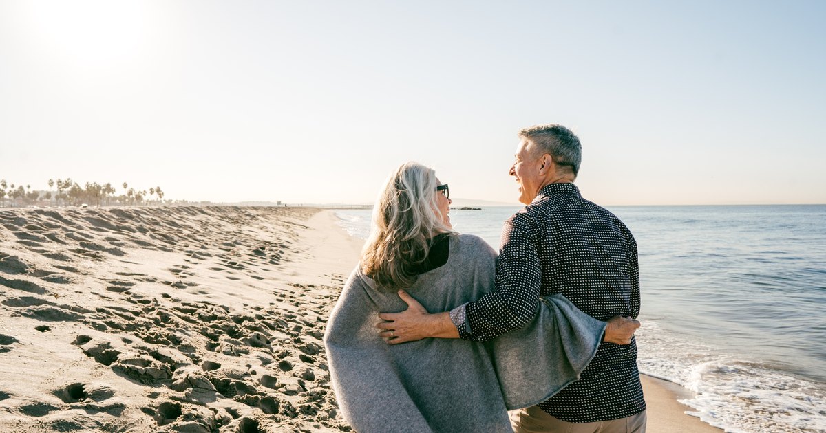 Un couple de seniors regarde la mer depuis une plage.