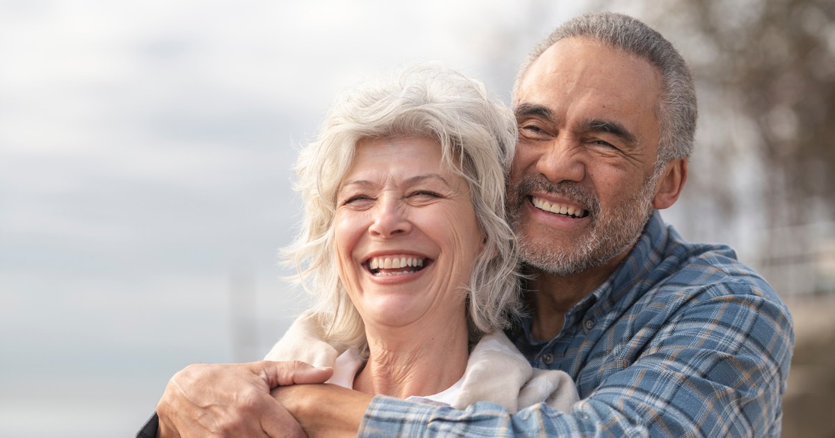 Un couple de seniors sourit en se tenant dans les bras.