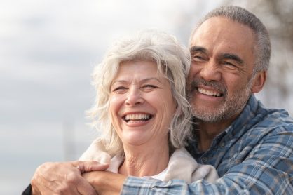 Un couple de seniors sourit en se tenant dans les bras.